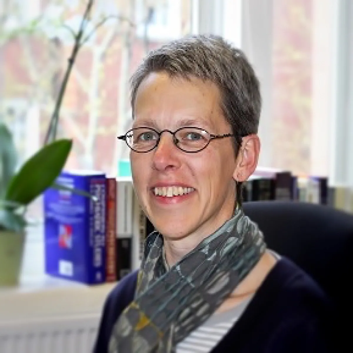 A woman with short hair and glasses smiling at the camera in an office setting.