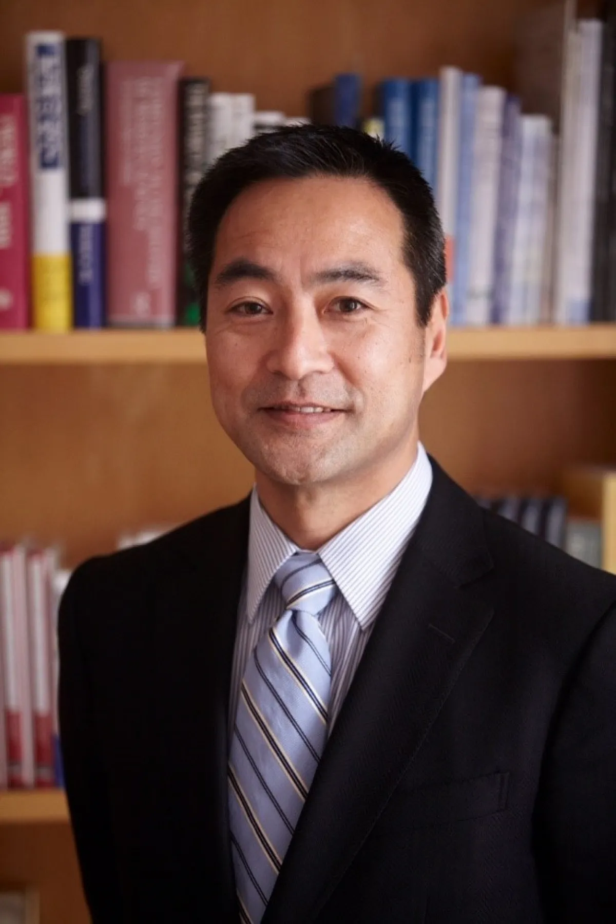A man in a business suit and striped tie smiling in front of a bookshelf.