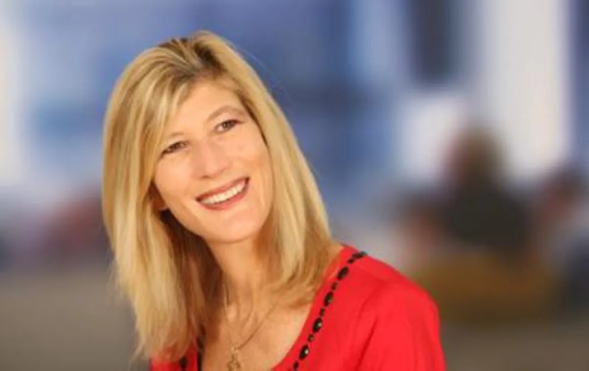 A woman with shoulder-length blonde hair smiling in a red blouse against a softly blurred background.