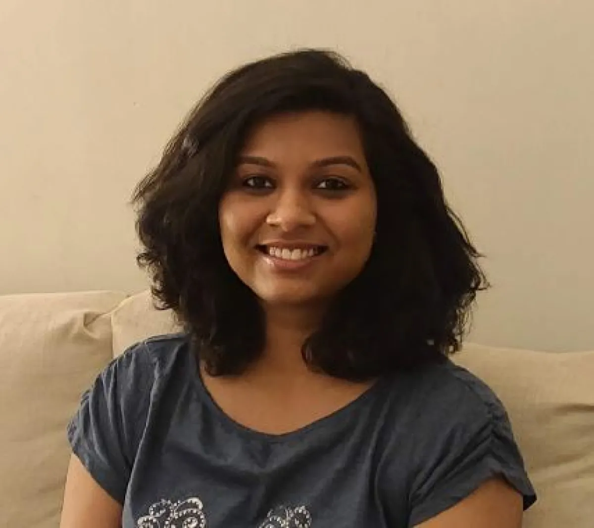 A smiling woman with shoulder-length curly hair sitting on a couch.