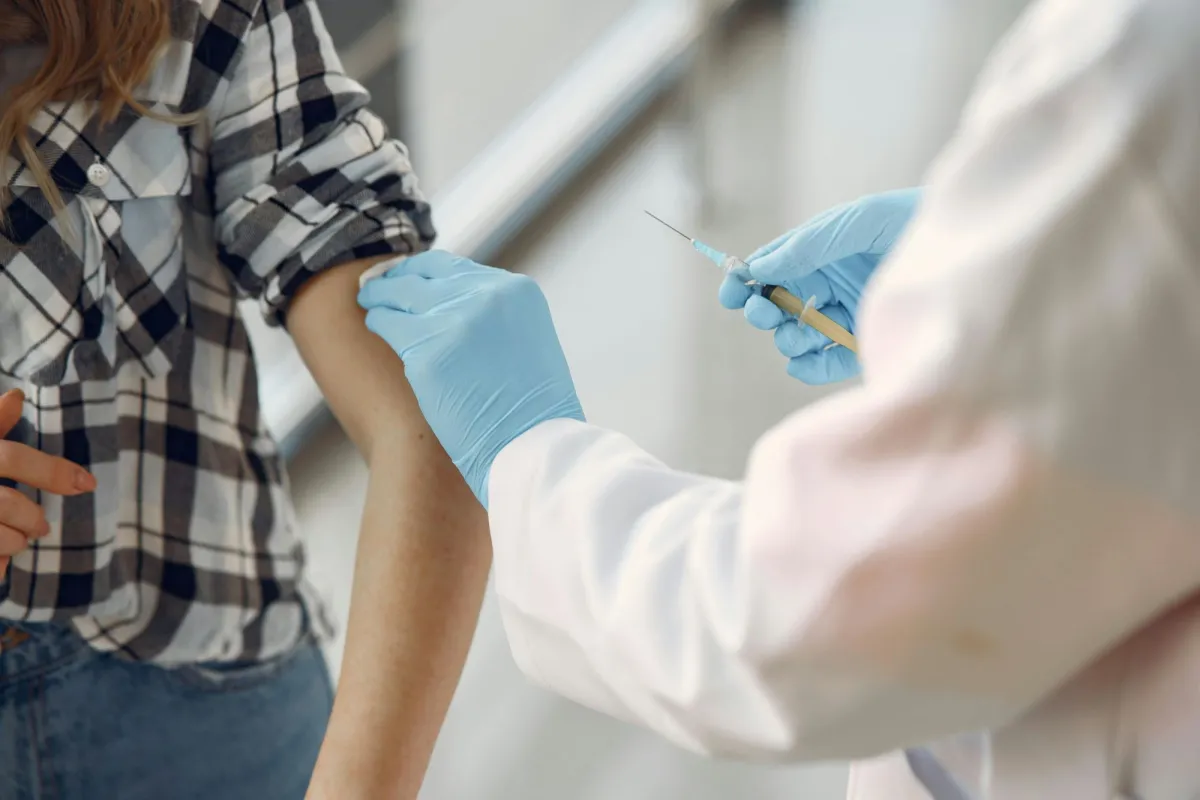 A healthcare worker in gloves administers a vaccination to a person wearing a plaid shirt.