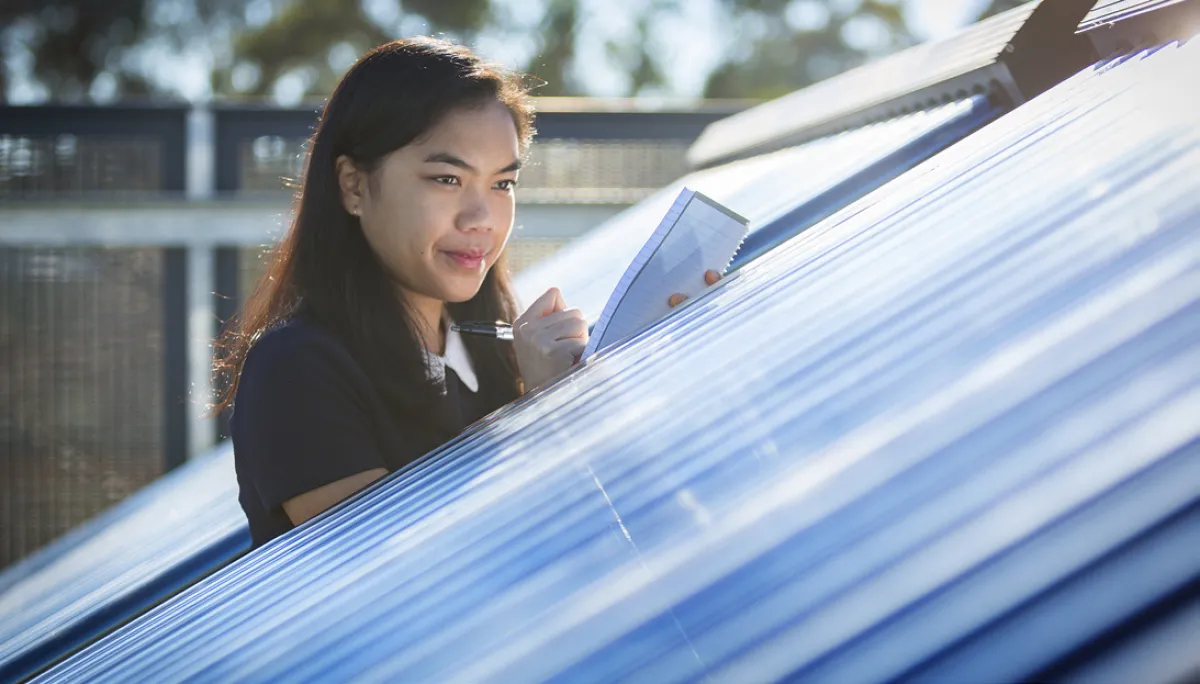 A woman examines solar panels while holding a clipboard and pen.