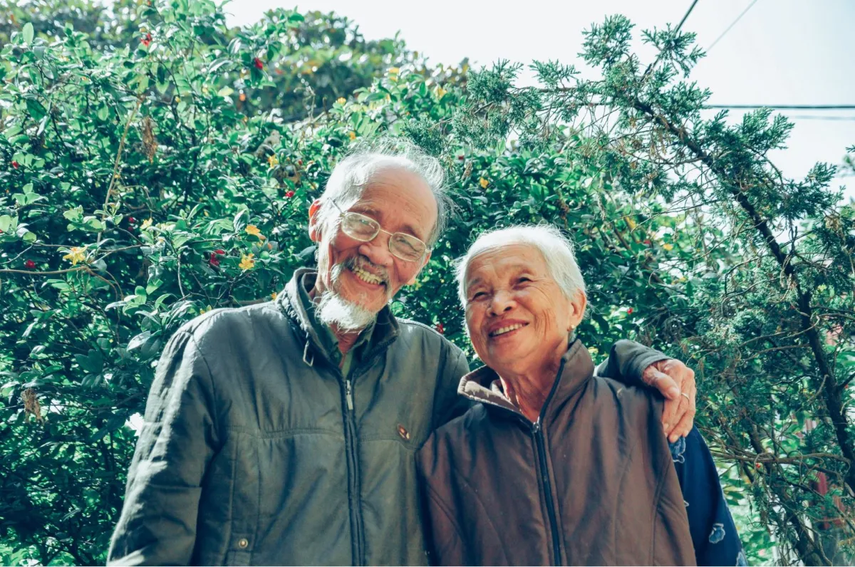 Two elderly men smiling and embracing in a lush garden.