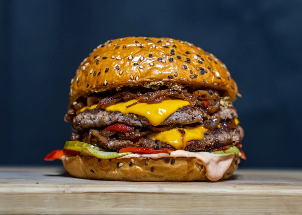 A double cheeseburger featuring sesame seed buns, loaded with grilled onions, bell peppers, and sauce.