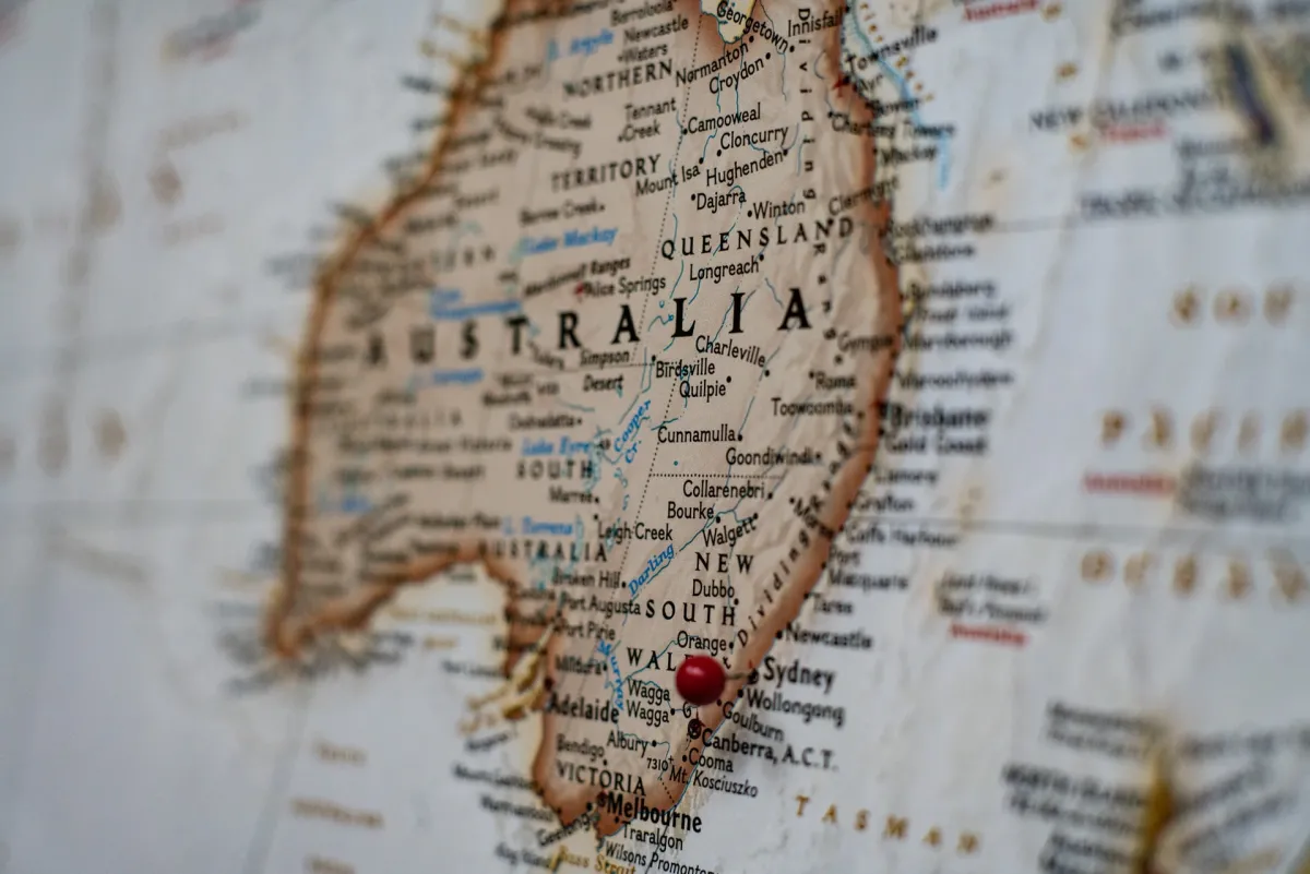 A close-up of a worn map focusing on Australia, with a red pin marking a location.