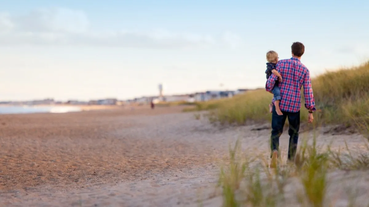 Father holding child while walking on beach
