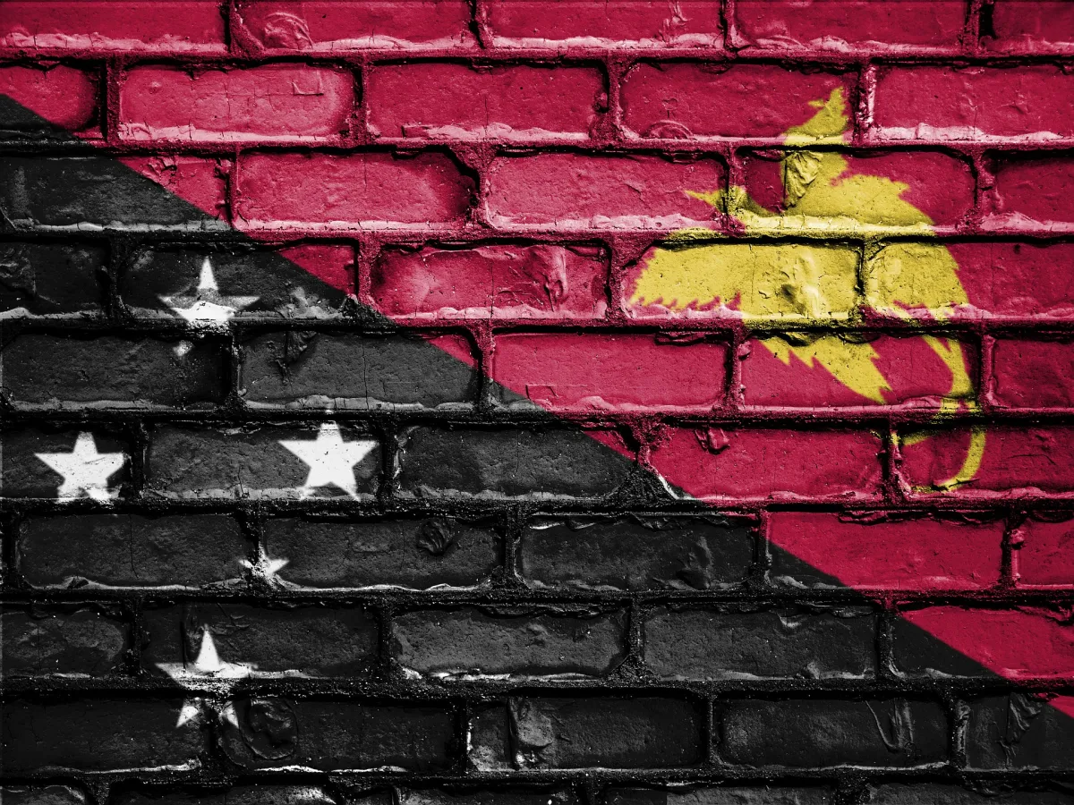 A brick wall painted with the flag of Papua New Guinea, featuring black and red sections divided diagonally with white stars on the black side and a yellow bird of paradise on the red side.