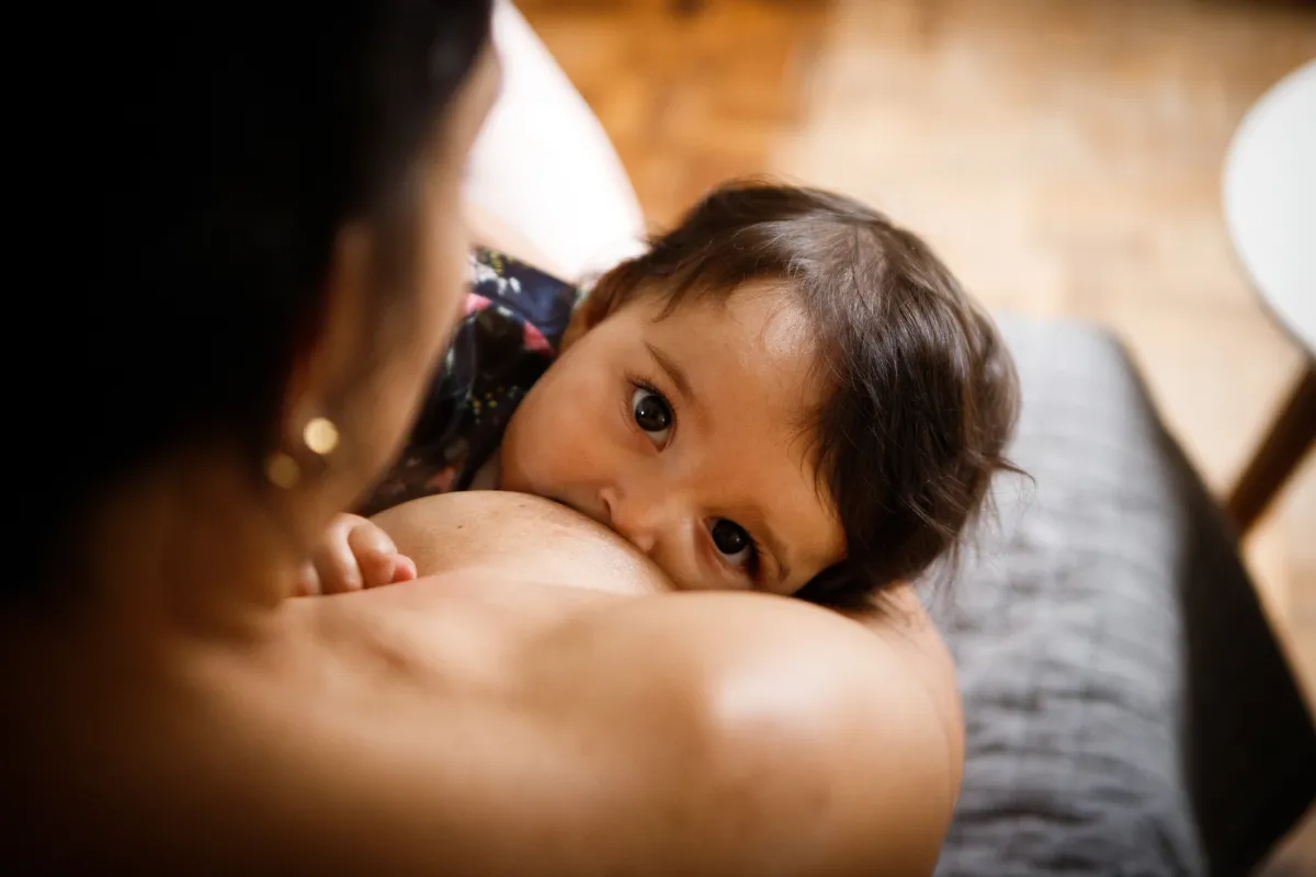 A baby gazes into the camera while breastfeeding.