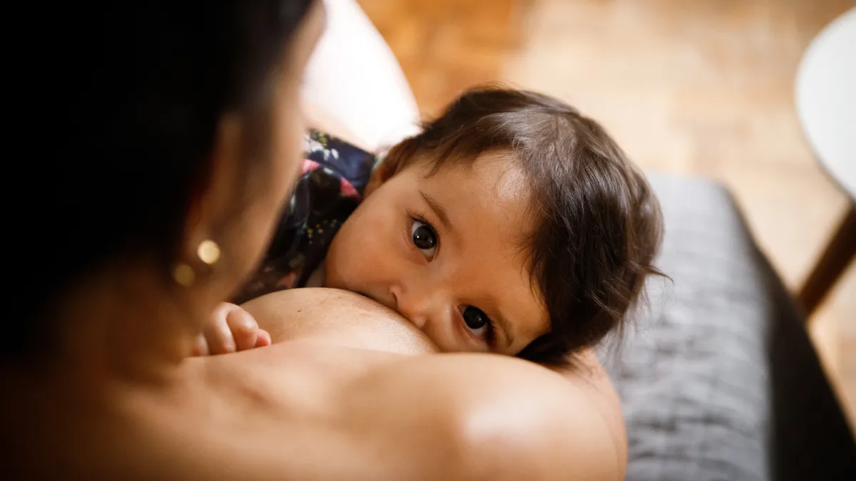 A baby is breastfeeding while making eye contact with the camera.