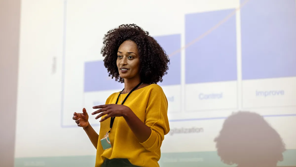 A woman presenting at a conference with a digital projection in the background.