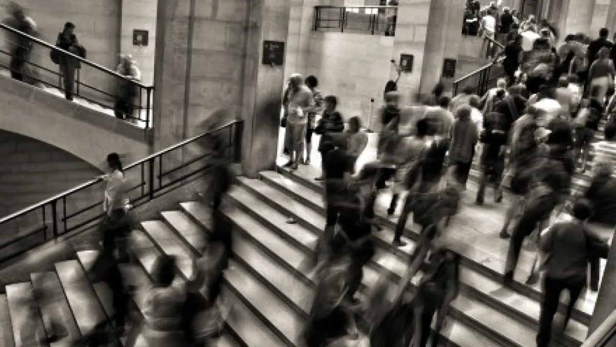 A black and white photo of a busy indoor staircase with many blurred people in motion.