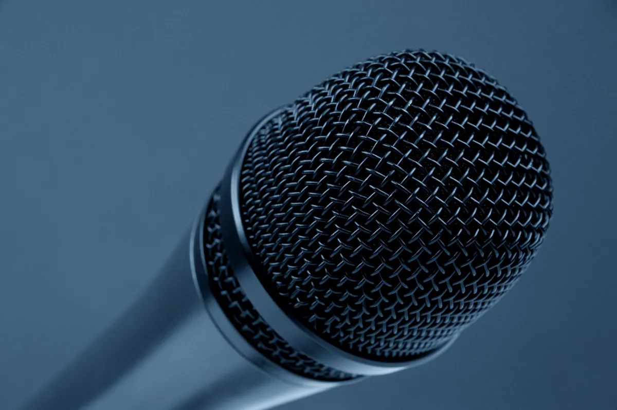 Close-up of a microphone with a detailed mesh grille on a gray background.