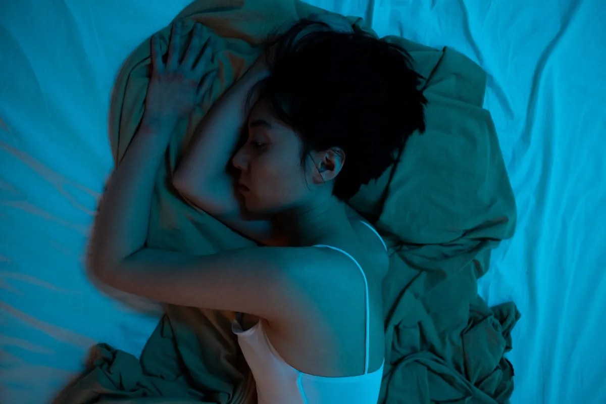 A woman sleeping in her bed under blue lighting.