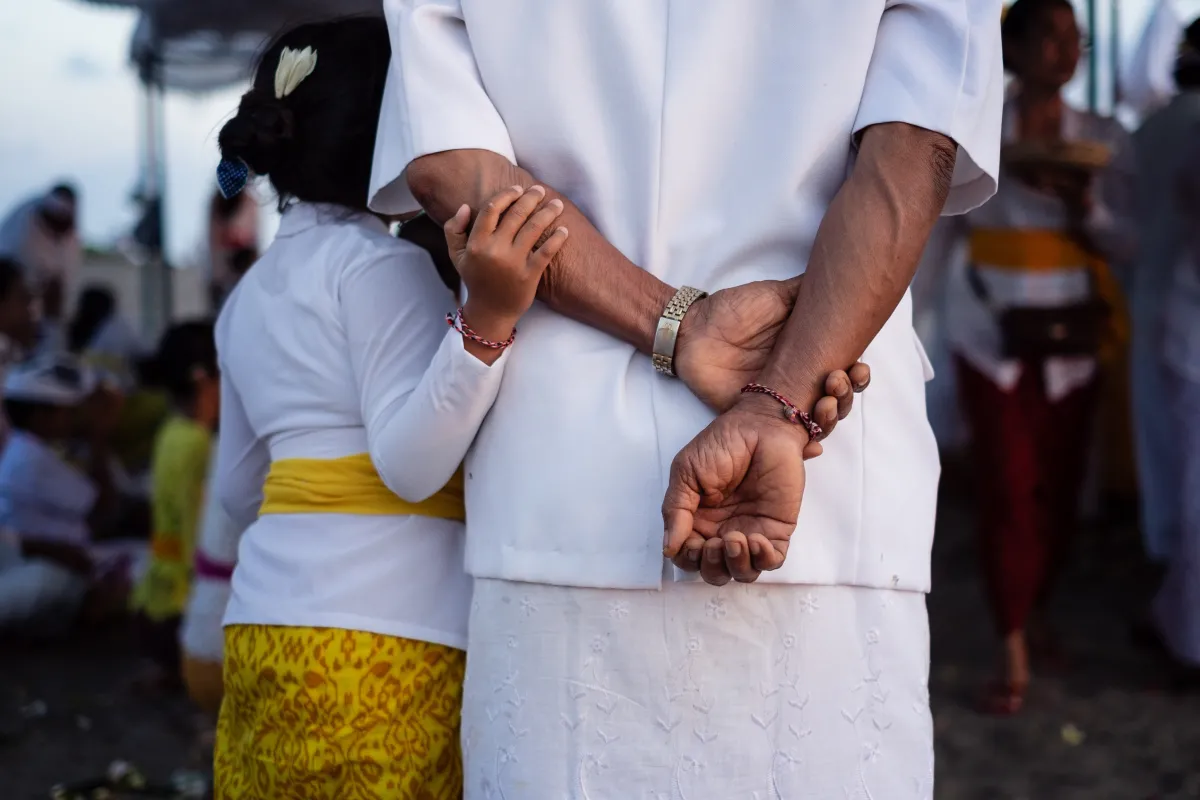 A close-up of two people holding hands, one in a white shirt and the other in a white top with a yellow skirt, at a crowded event.