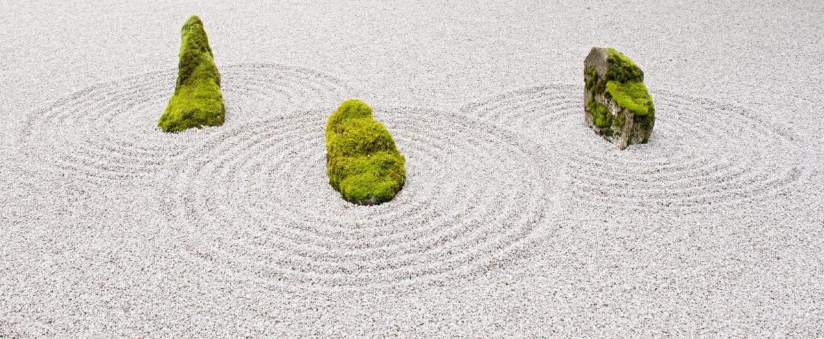 A Zen garden featuring several moss-covered rocks set in patterns of raked white gravel.