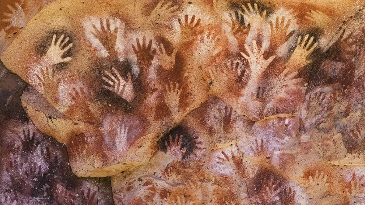 &quot;Cave wall adorned with multiple prehistoric hand stencils in red and orange pigments.&quot;