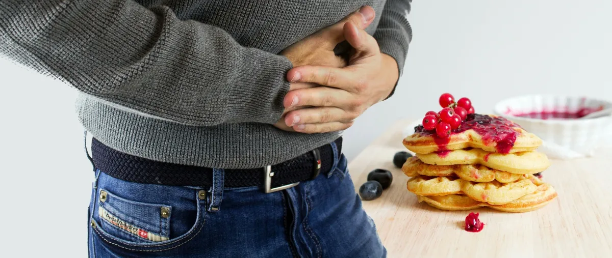 A person clutching their stomach with a plate of pancakes topped with berries in the background.