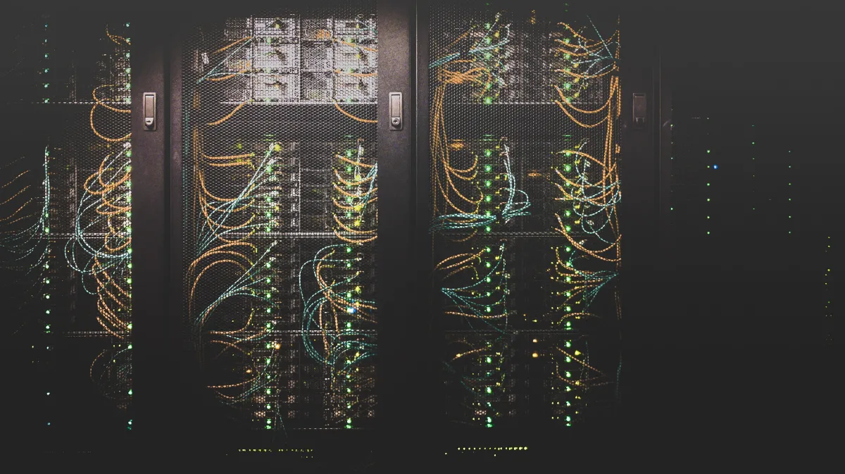 A view of a dark server rack illuminated by numerous colorful network cables and flashing LED lights.