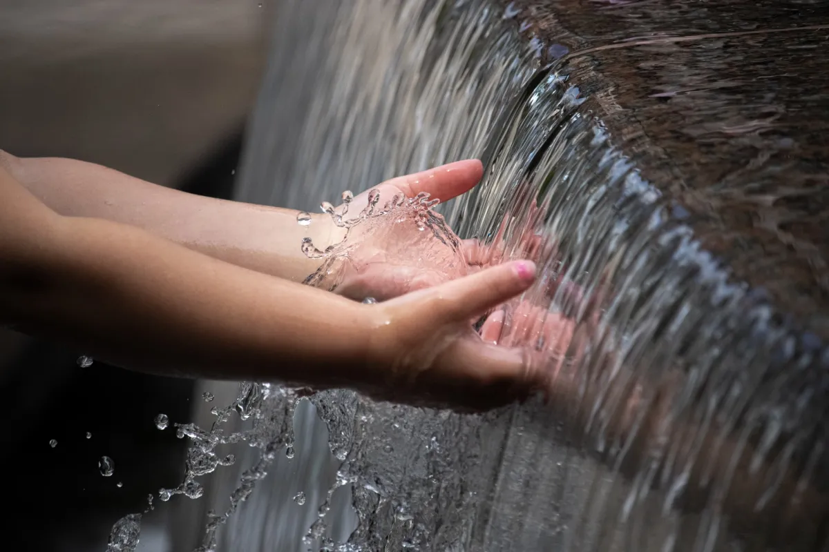 A person's hands interacting with splashing water from a fountain.