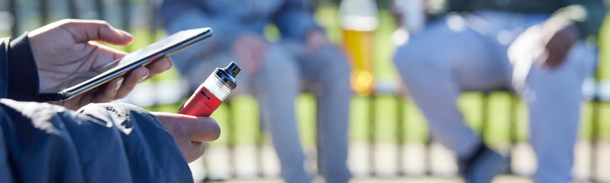 Image shows a person holding a vape and their mobile phone.