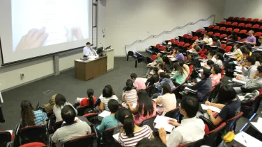 A lecturer speaks to a crowd of students in a large university auditorium.