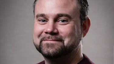 Portrait of a man with a beard smiling gently, wearing a maroon shirt.