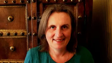 A woman smiling in a teal shirt in front of a decorative wooden door with studs.