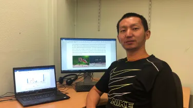 A man seated at a desk with two laptops, one displaying a graph and the other showing a document with images of athletes.
