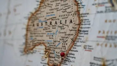 A close-up of a worn map focusing on Australia, with a red pin marking a location.