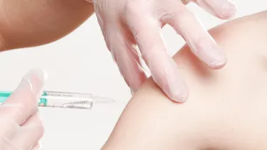 A person in gloves administering an injection into another person's upper arm.