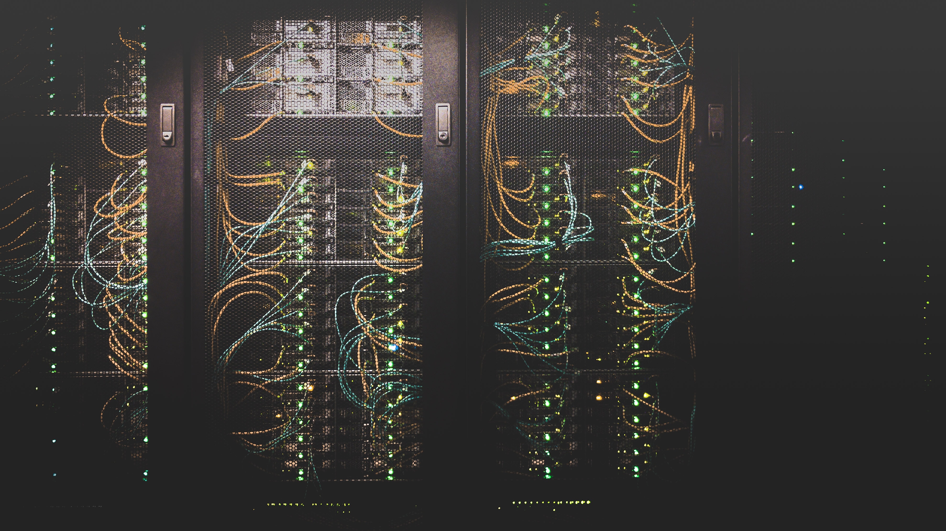 A view of a dark server rack illuminated by numerous colorful network cables and flashing LED lights.